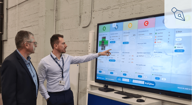 SABCA blog Deux hommes en discussion devant un grand écran interactif affichant un tableau de bord SQCDP digitalisé. L’un d’eux, en chemise claire, pointe un indicateur sur l’écran tandis que l’autre l’observe attentivement. L’écran présente des données de performance industrielle (sécurité, qualité, délais, coûts, personnel, environnement) utilisées pour le pilotage quotidien de la production chez SABCA, avec l’interface développée par Pingflow. L’image illustre un moment de management visuel en contexte industriel.